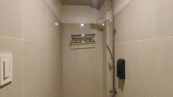 Un petit espace de douche carrelé, équipé d’un pommeau de douche à main, d’un porte-serviettes et d’un distributeur de savon.