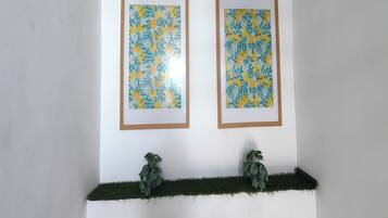 Dos obras de arte florales enmarcadas sobre una pared blanca, con dos plantas en macetas en un estante verde debajo.