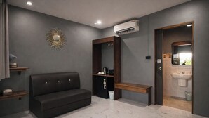 Una habitación moderna con un sofá de cuero oscuro, un banco de madera, una pequeña mesa con lámpara y una estantería empotrada.