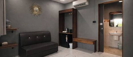 A modern room with a dark leather sofa, a wooden bench, a small table with a lamp, and a built-in shelf.
