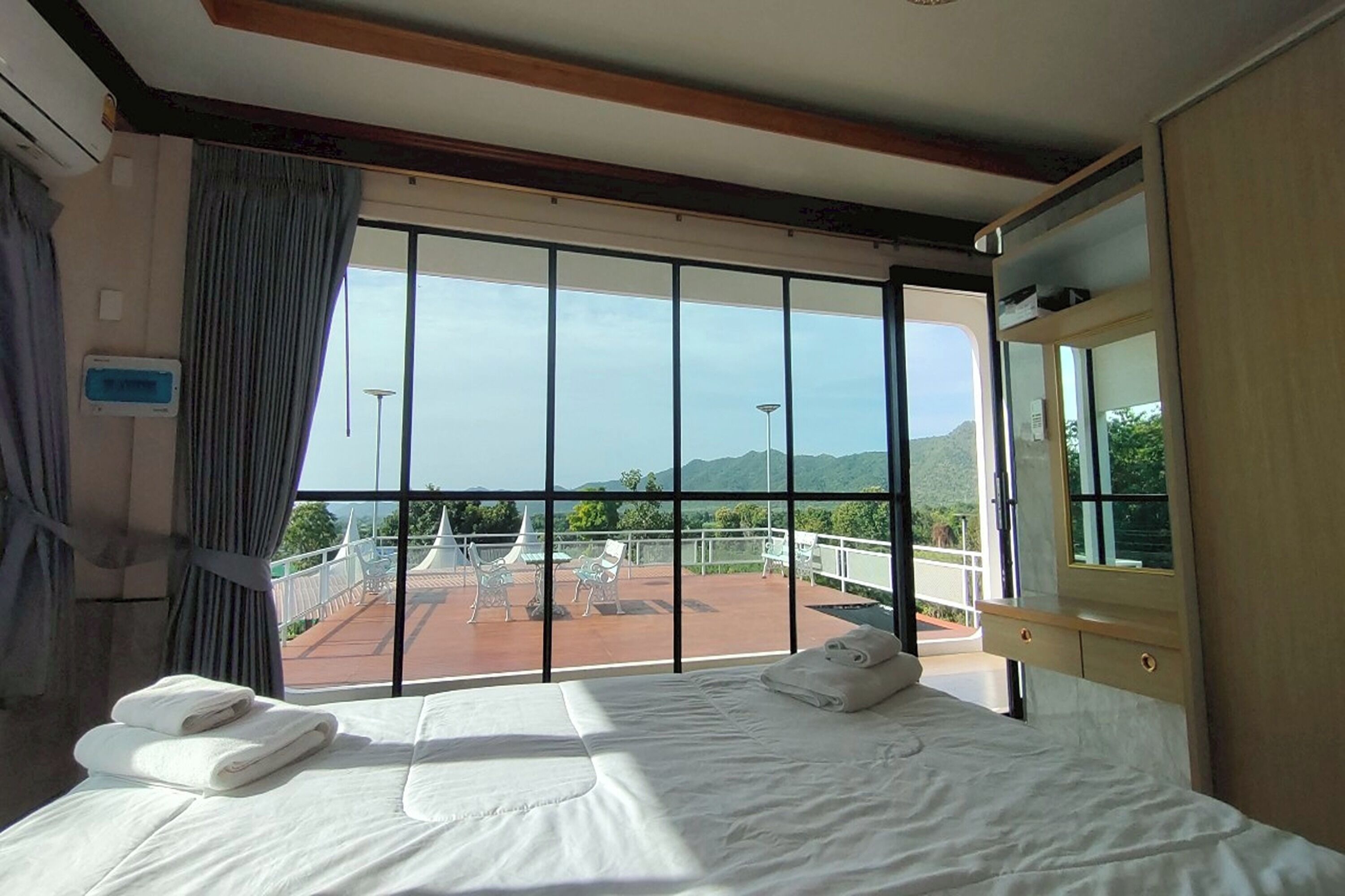 A hotel room with a large window, a bed, and a balcony with chairs.