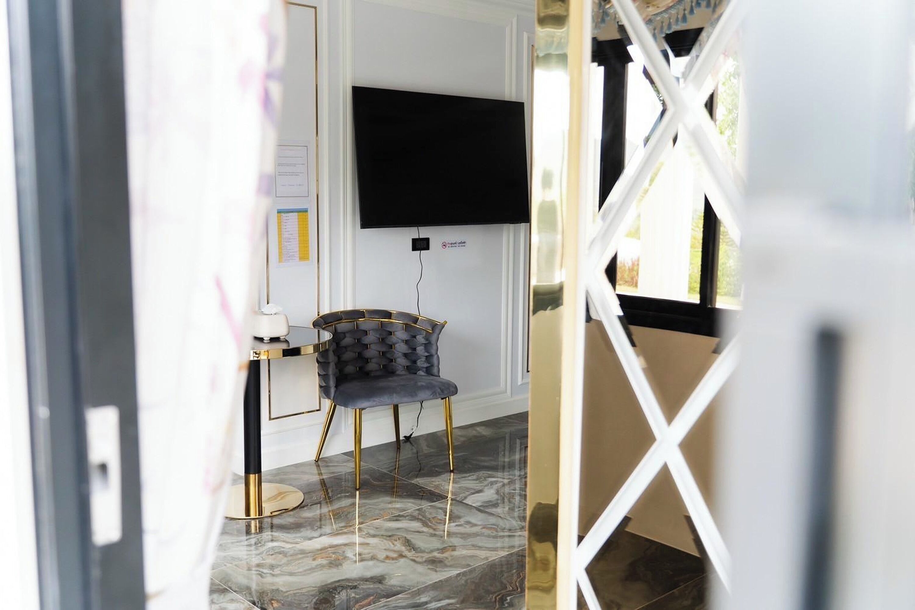 A room with a flat-screen TV mounted on the wall, a dark upholstered chair, a small round table, and a marble floor.