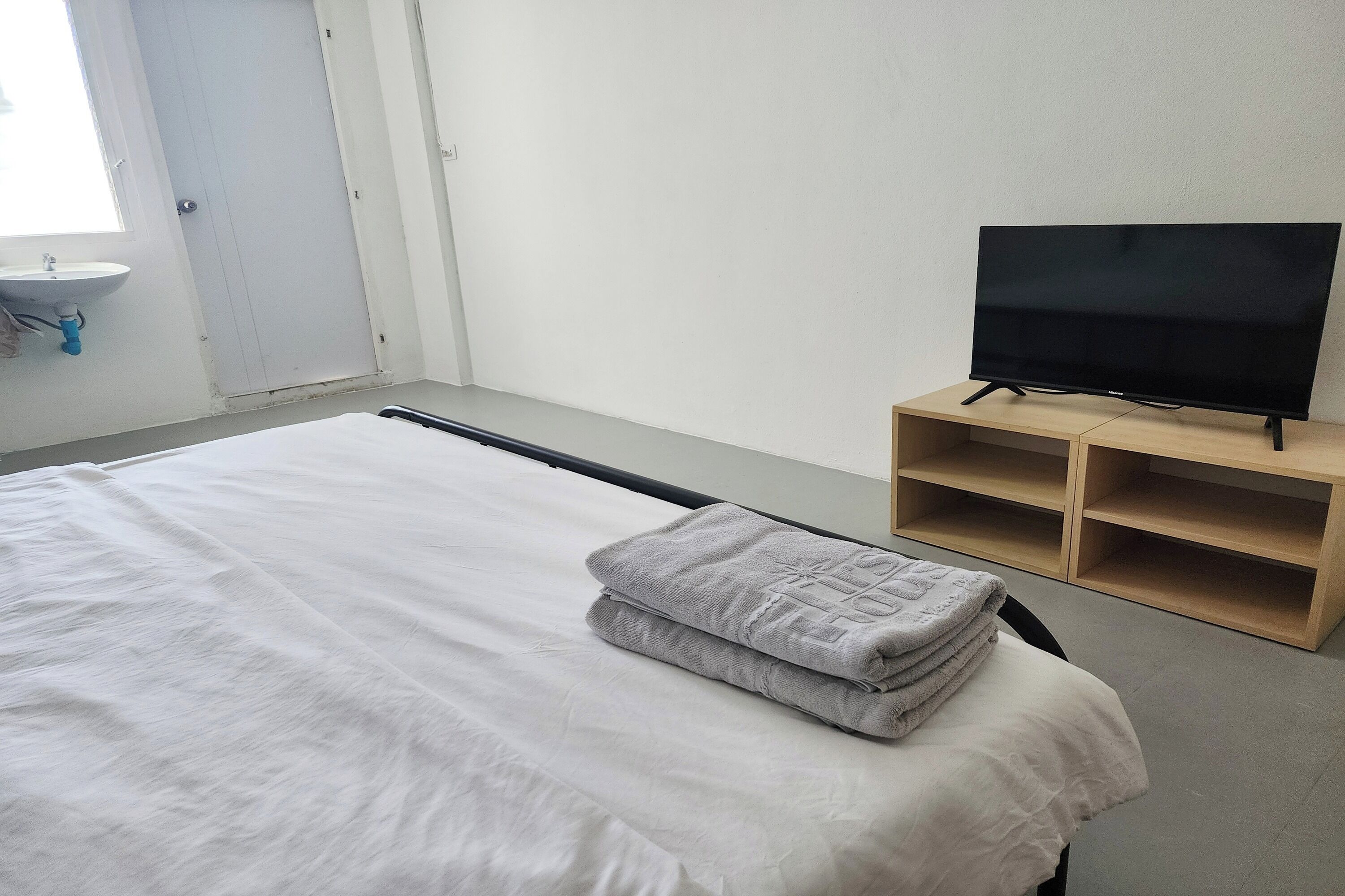 Une chambre d’hôtel avec un lit, un téléviseur posé sur un meuble en bois, un lavabo et une fenêtre.
