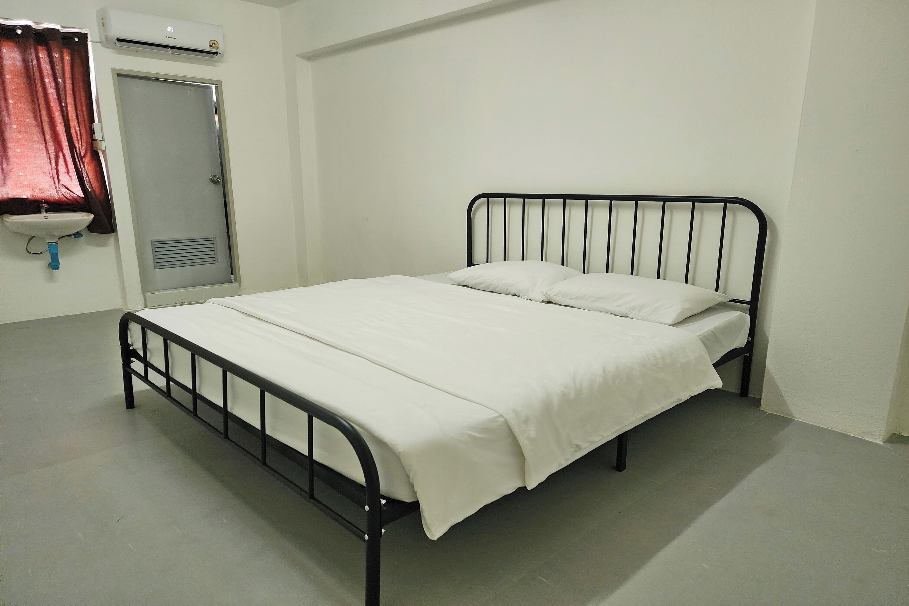 A simple, clean room with a single bed, a door, and a small sink.