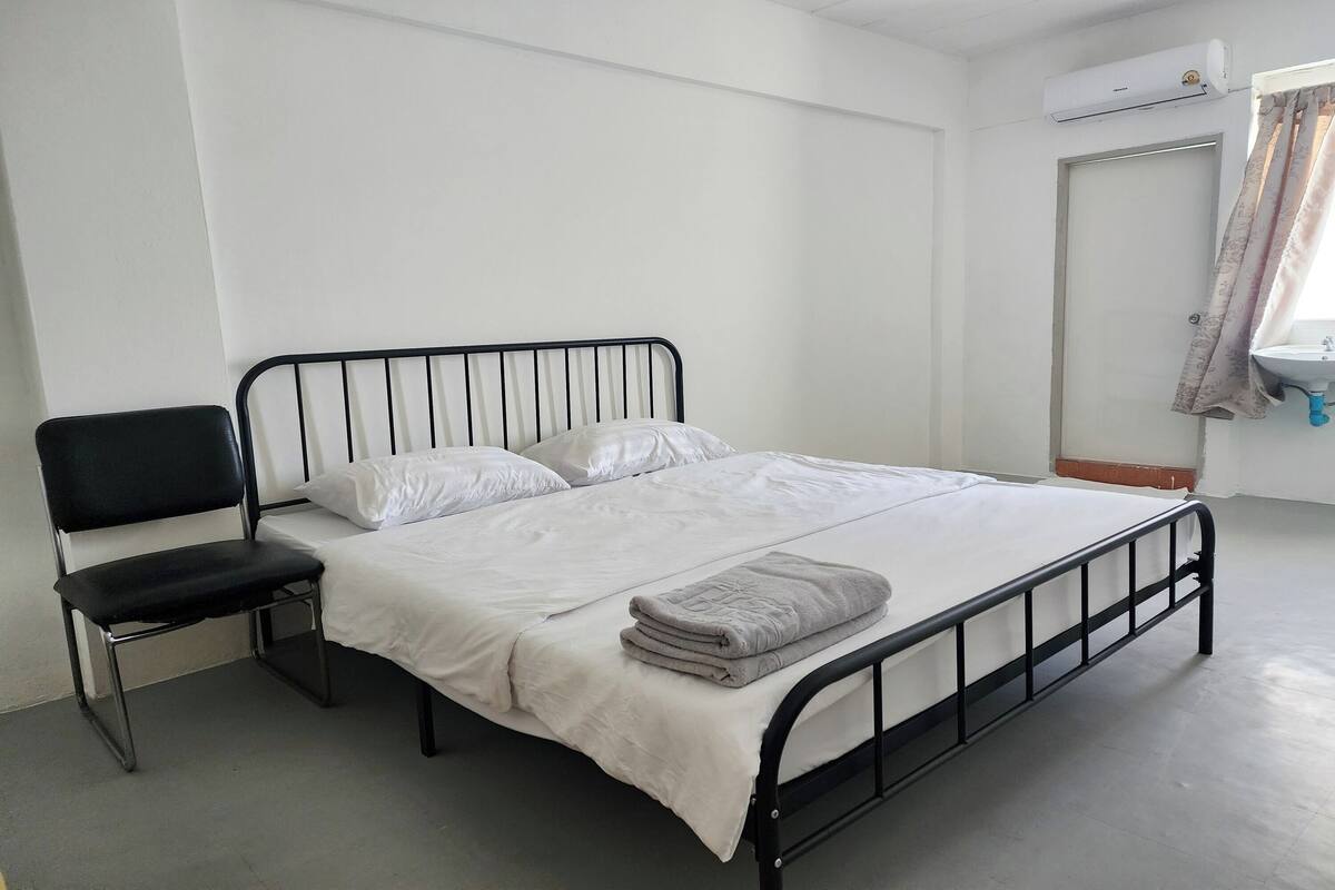 A bed with a black metal frame, white bedding, a folded grey blanket, and a black chair.