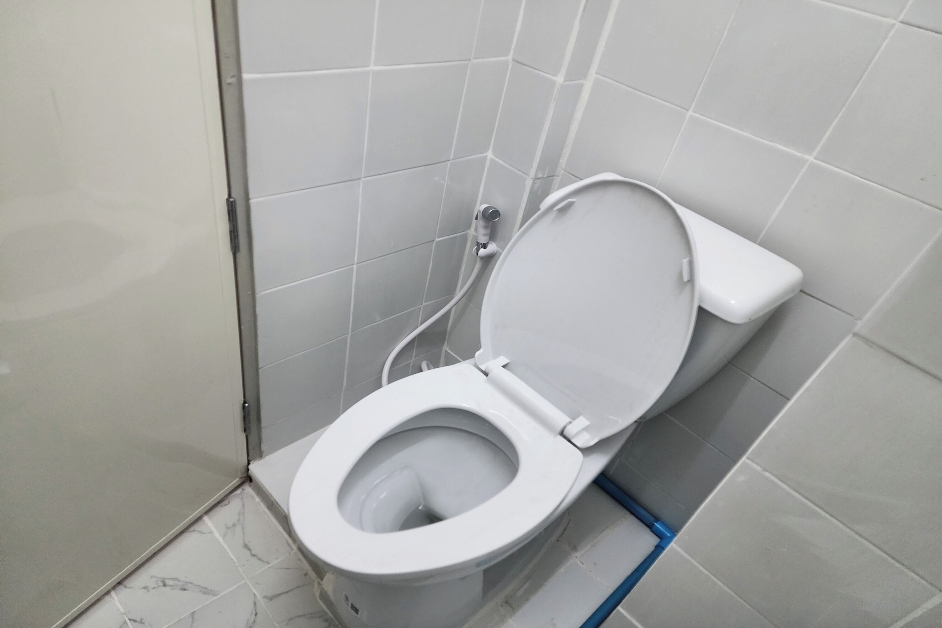 Des toilettes blanches avec un abattant fermé, dans une salle de bain aux murs et au sol recouverts de carreaux blancs.