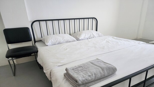 A bed with white linens and a grey towel, a black metal headboard, and a black chair. - Toucan Garden (Bang Phli)
