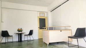 Ein Zimmer mit Schreibtisch, zwei Stühlen, einem kleinen Tisch mit Blumen und einer Tür mit einem Bilderrahmen.