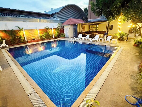 Una piscina con bordes de azulejos, rodeada de sillas de descanso y plantas en macetas.