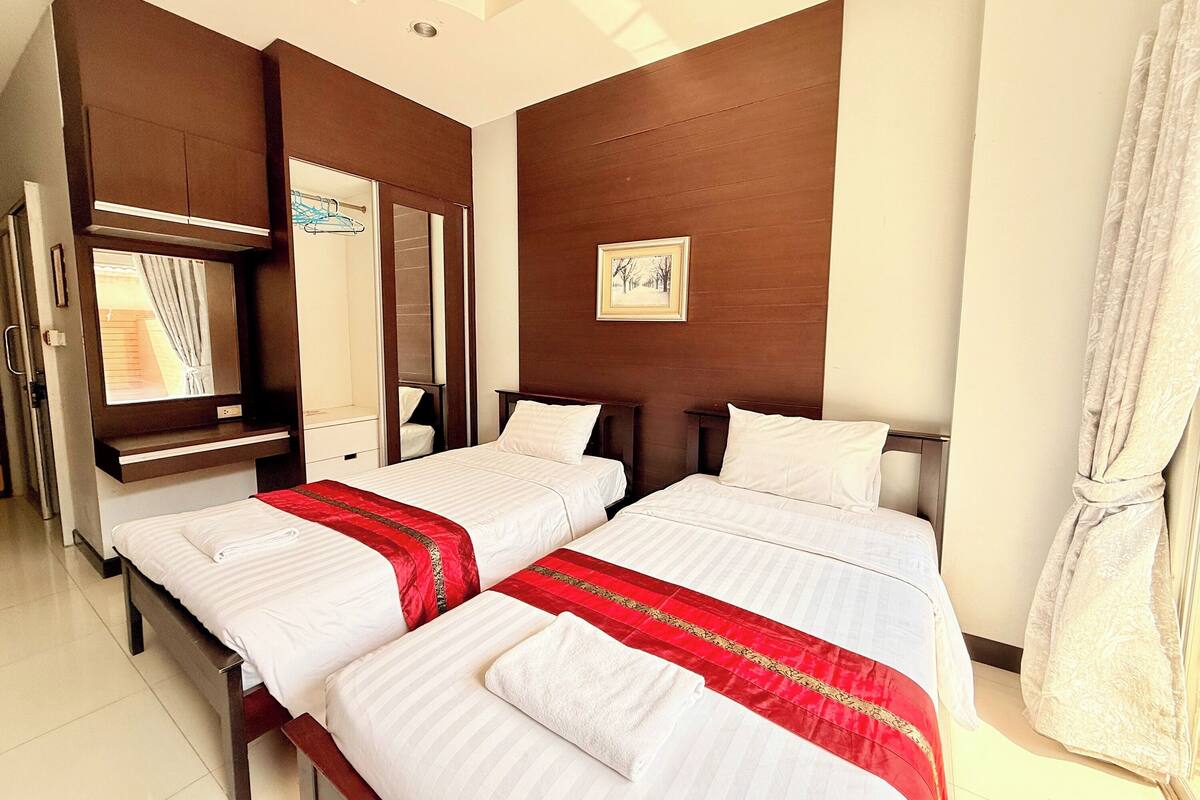 A hotel room with two beds, a large mirror, a painting on the wall, and a window with curtains.