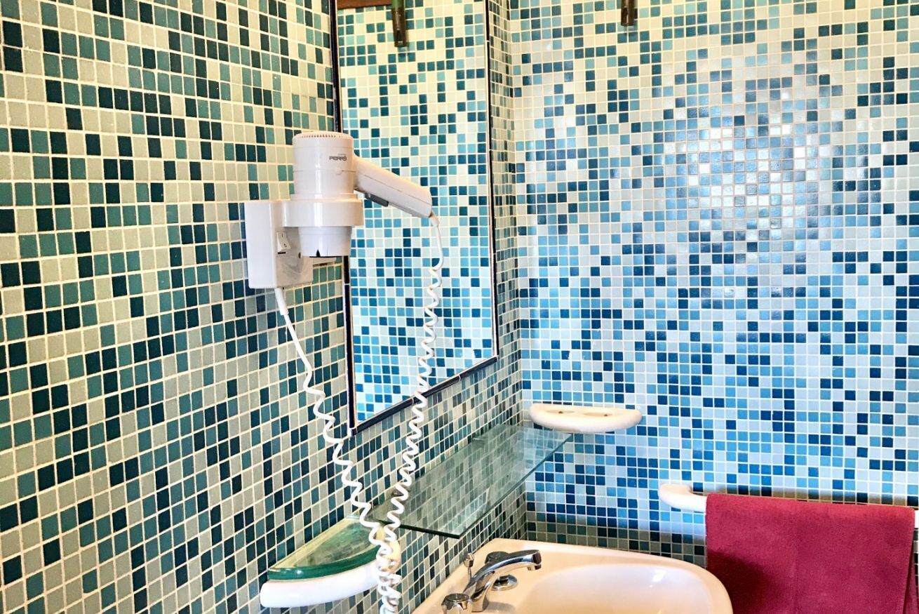 A bathroom with mosaic tile walls, a white sink, a mirror, and a hairdryer.