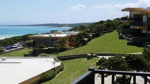 A coastal property with a view of the sea, a grassy area, and a building with a balcony. - Functional 28 sq m room.Comprising a double bed, two single beds, and a private bathroom with shower, bidet, and hairdryer. The room also features an outdoor space with a sea view, a patio or terrace, and a table and chairs. Breakfast is included in the  (Stintino)
