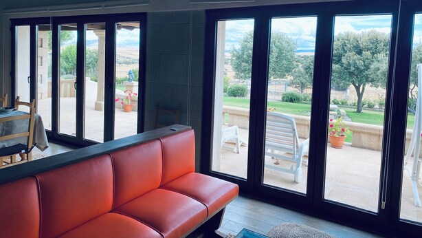 Quarto com sofá de couro vermelho, grandes portas de correr de vidro e vista para um jardim.