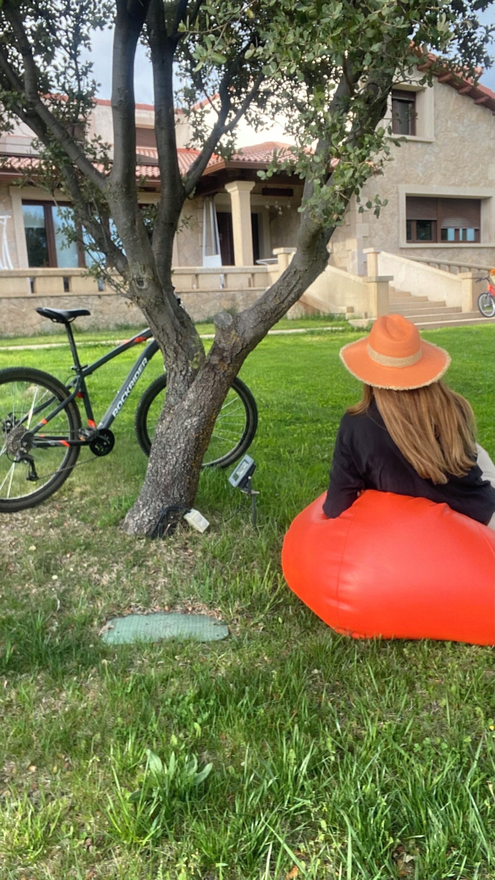 Una persona sentada en un sillón de mimbre rojo debajo de un árbol, con una bicicleta estacionada cerca.