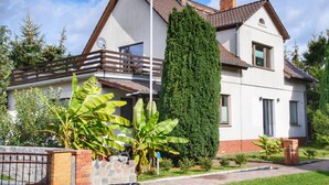 A two-story house with a balcony, a tall coniferous tree, and a variety of plants. - Familienurlaub in Monkebude (Monkebude)