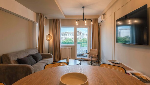 Un salon moderne avec un canapé, une table à manger agrémentée d’un saladier, un téléviseur et une vue sur les immeubles par la fenêtre.