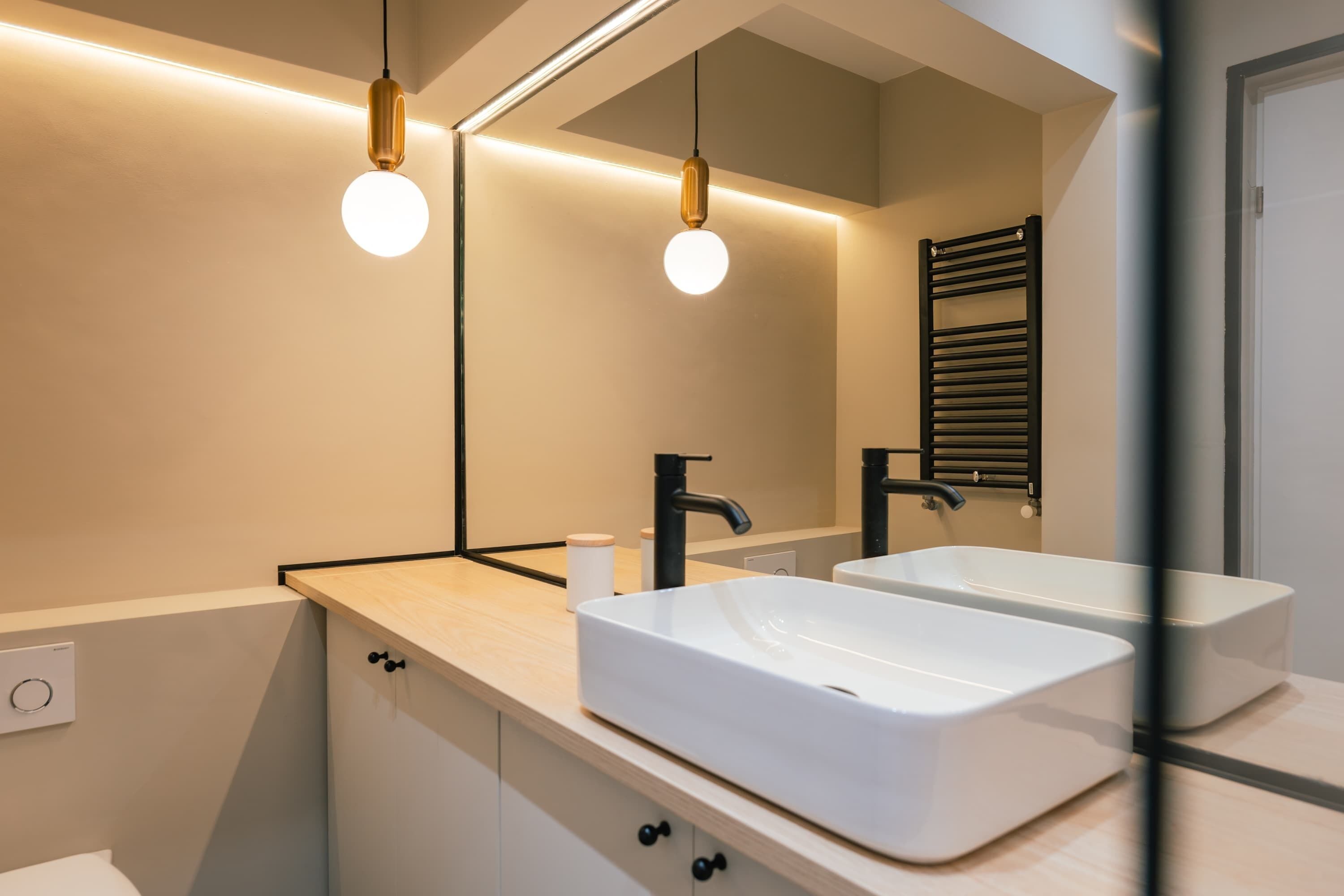 Un baño moderno con un espejo grande, dos lavamanos e iluminación colgante.
