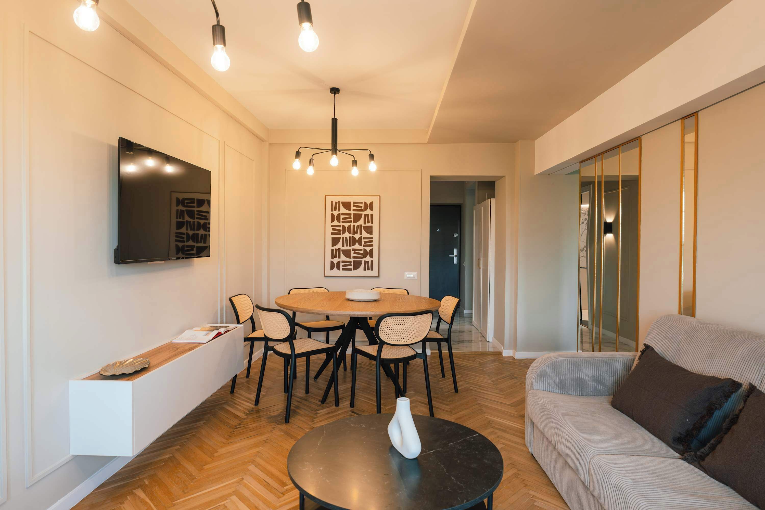 A modern living room with a round dining table, chairs, a sofa, a coffee table, and a TV mounted on the wall.