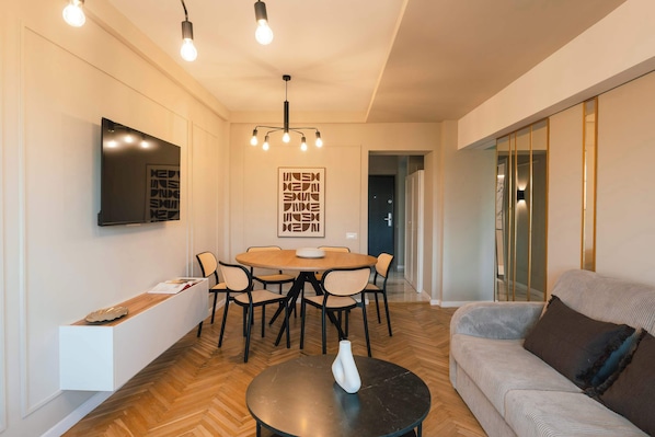 Un salon moderne avec une table de salle à manger ronde, des chaises, un canapé, une table basse et un téléviseur fixé au mur.