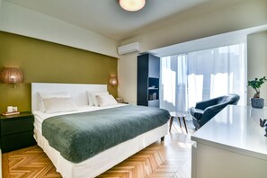 Una habitación de hotel moderna con una cama, mesitas de noche, un escritorio, una silla y un ventanal grande.