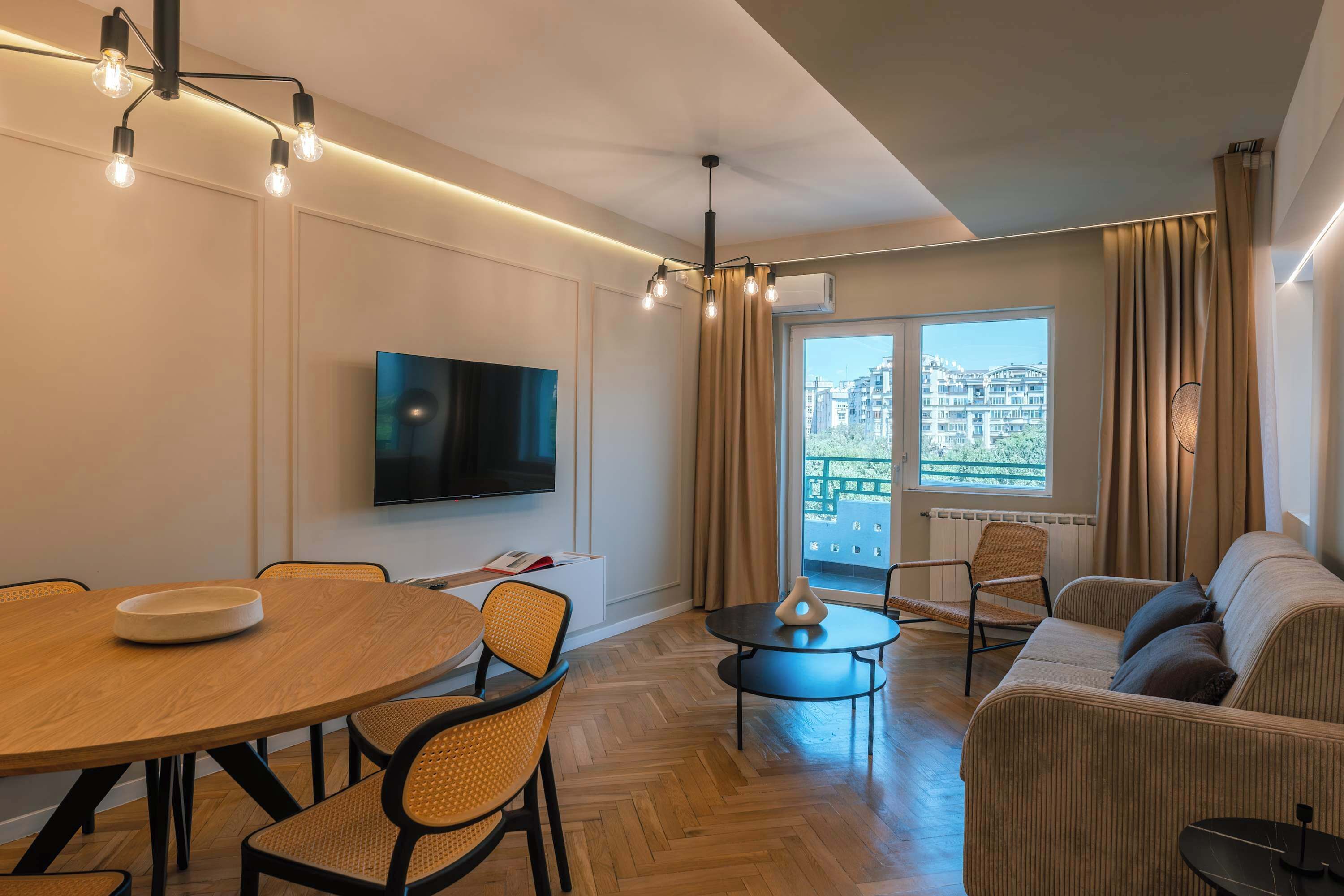 A modern living room with a dining area, a sofa, a TV, and a view of buildings through the window.