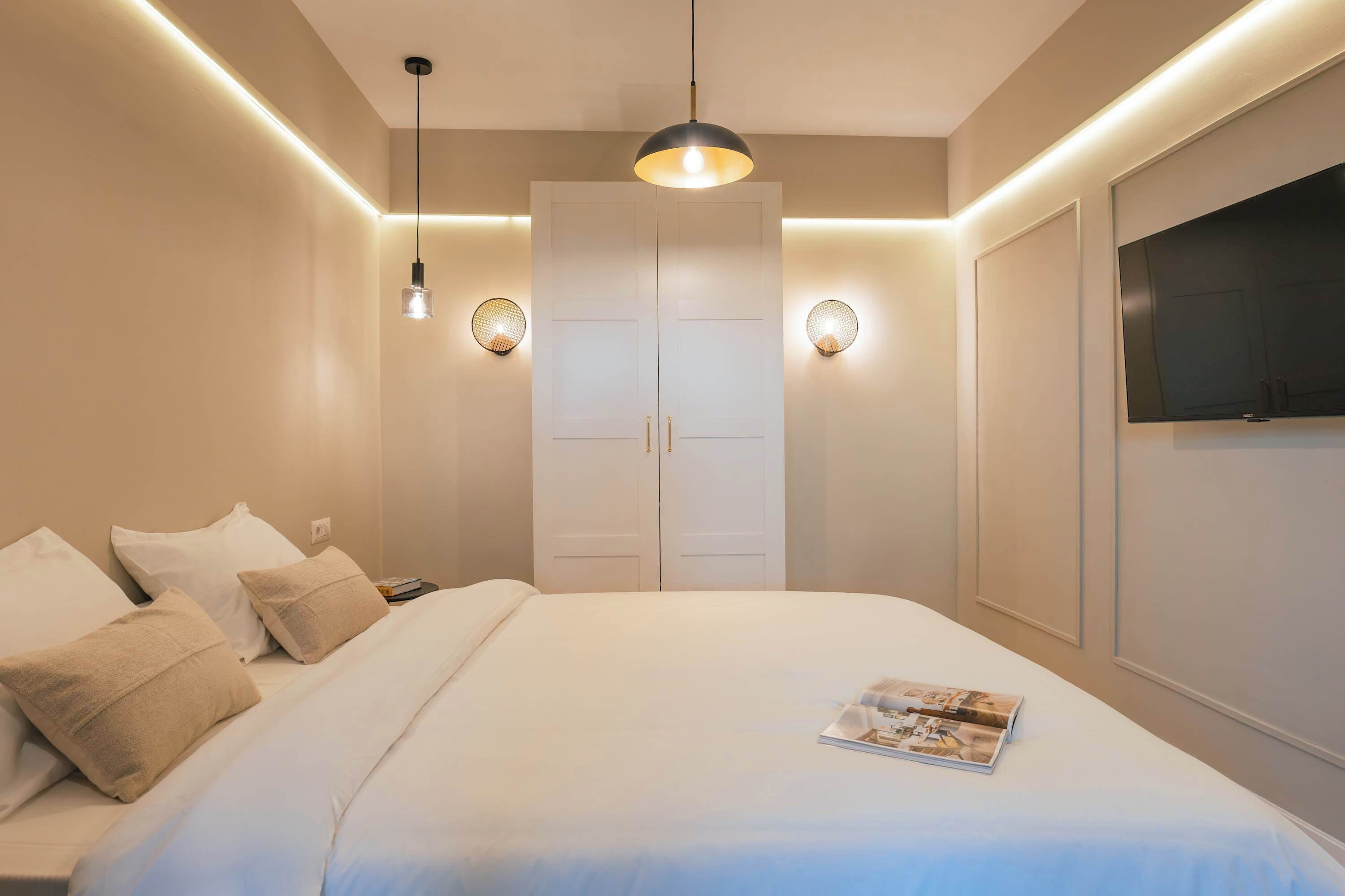 A hotel room with a bed, a wardrobe, a television, and wall-mounted lighting.