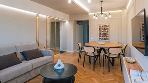 Un salon moderne comprenant un canapé, une table basse ronde, une table à manger avec des chaises et un téléviseur fixé au mur.