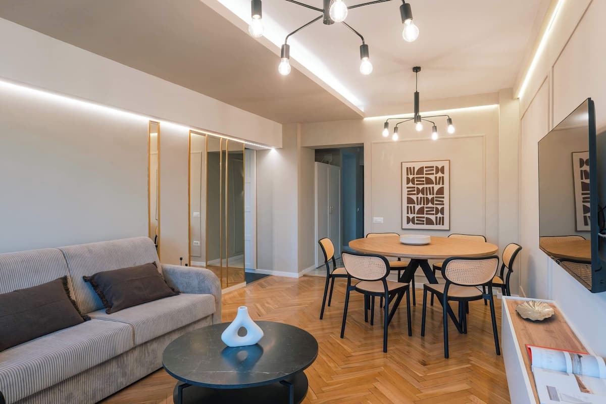 Un salon moderne comprenant un canapé, une table basse ronde, une table à manger avec des chaises et un téléviseur fixé au mur.