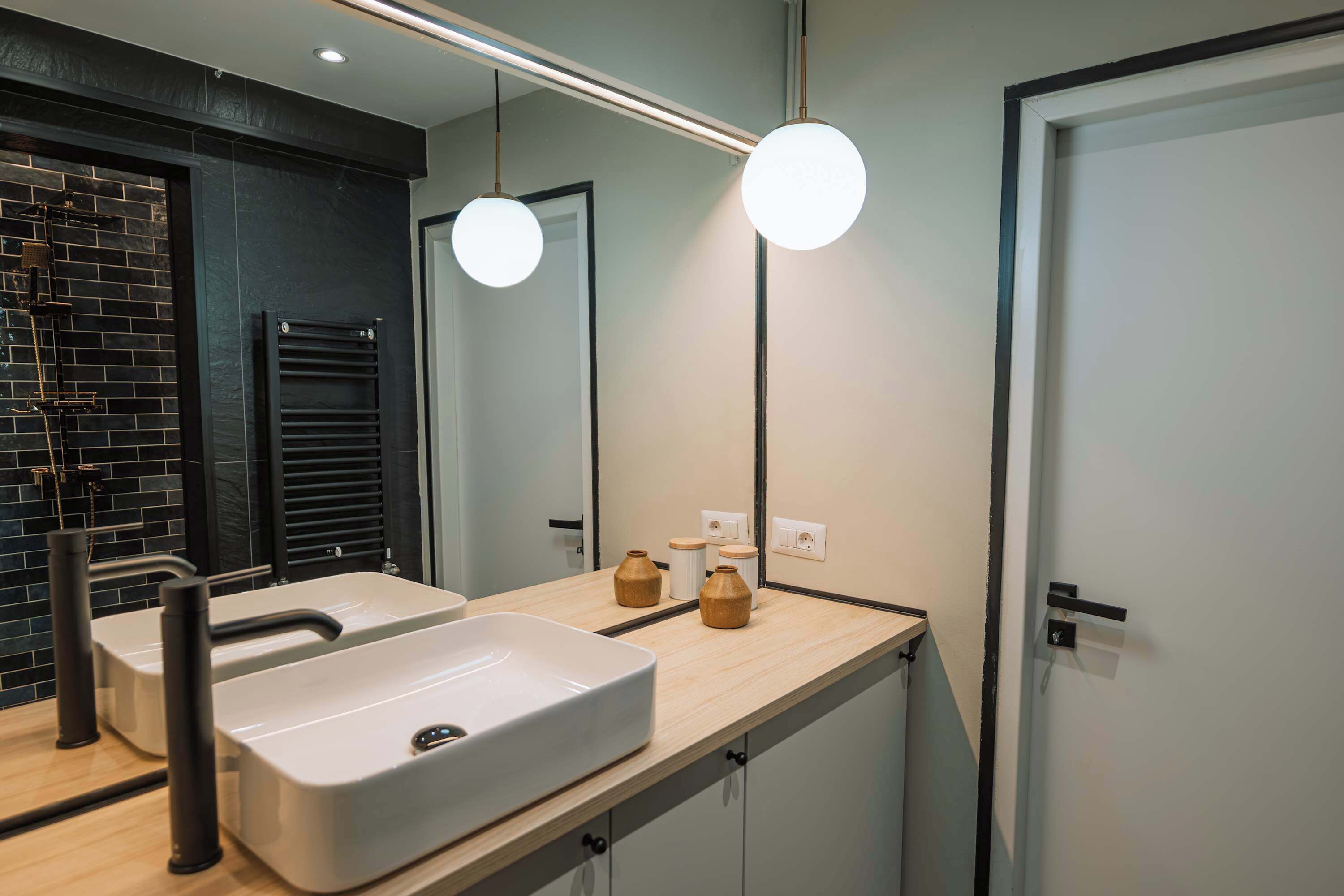 A modern bathroom with a large mirror, two round lights, a beige sink, and a black towel rack.