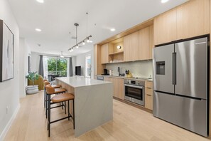 Une cuisine moderne dotée d’un grand îlot central, d’appareils électroménagers en acier inoxydable, de meubles de rangement en bois et d’un coin bar avec des tabourets.