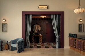 A room with a checkered floor, a fireplace, a mirror, and a sign indicating an elevator. - 1BR Suite w/ Private Balcony | Pool + Terrace + Restaurant | The Code (Austin)