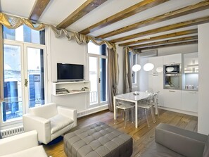 A modern living room with a flat-screen TV, white sofas, a dining table with chairs, and a kitchen area with a microwave and oven. - La Dolce Sosta – Elegant Retreat Steps from St. Mark’s Square (Venezia)