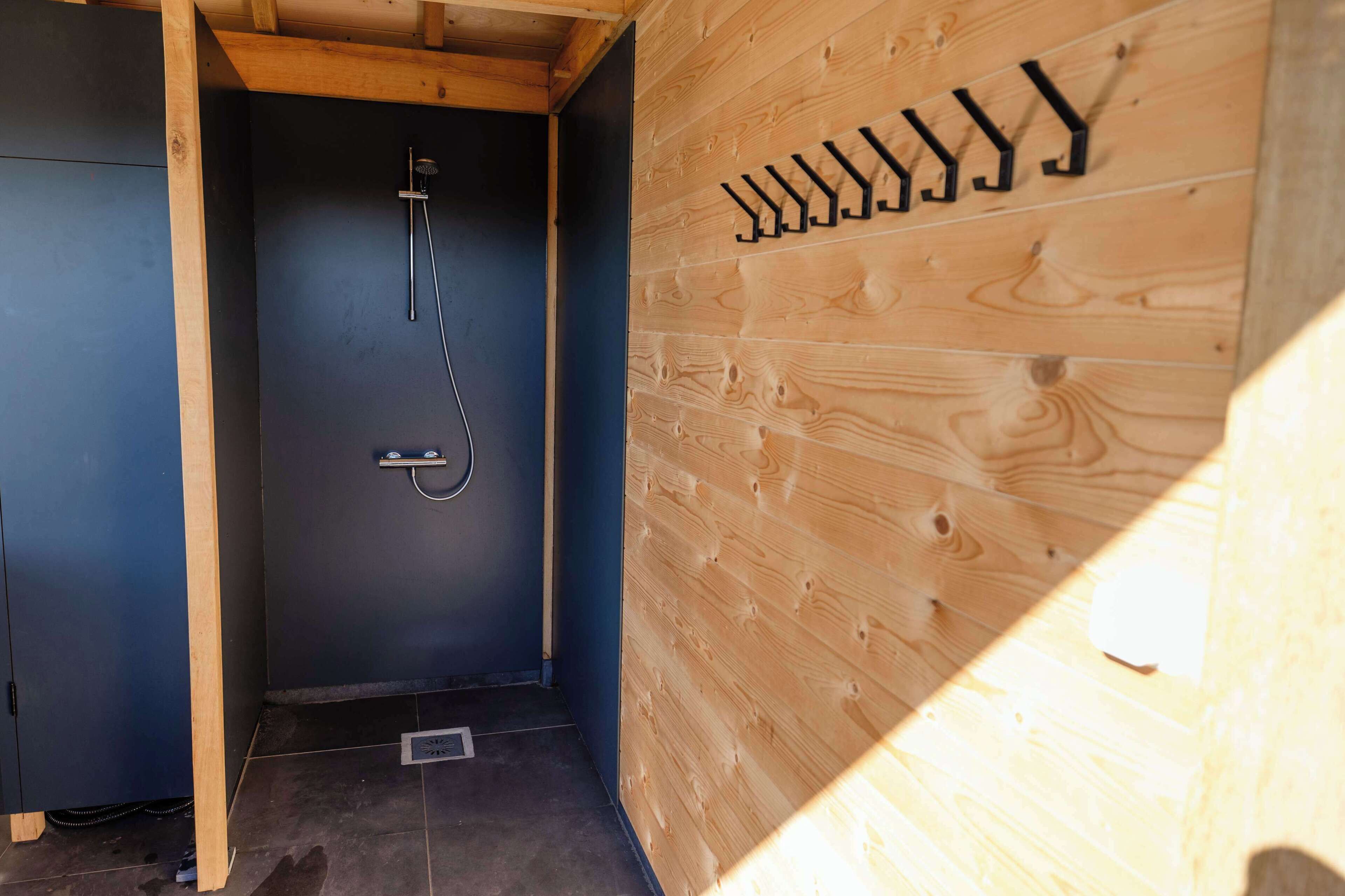 A wooden cabin interior with a shower, a dark door, and a wall-mounted coat rack.