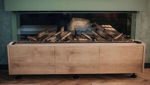 Une cheminée moderne dotée d’un foyer en verre, d’un meuble en bois en dessous et d’une télécommande placée sur le meuble.