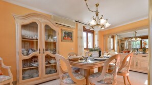 Ein Esszimmer mit einem Holzkabinett voller Geschirr, einer Chandelierleuchtre und einem großen Spiegel, der den Raum widerspiegelt.