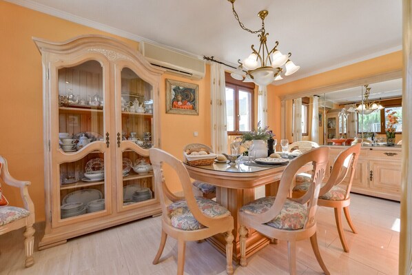 Une salle à manger avec un buffet en bois rempli de vaisselle, un lustre et un grand miroir qui reflète la pièce.