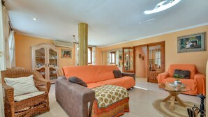 Ein geräumiges Wohnzimmer mit einem großen orangefarbenen Sofa, einem Korbsessel und einem Glastisch.