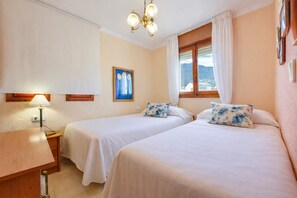 Une chambre d’hôtel avec deux lits, une table de chevet, une lampe, un tableau, une fenêtre avec des rideaux et un lustre.