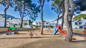 Ein Spielplatz mit Schaukeln und Rutschen, umgeben von Bäumen und Gebäuden.