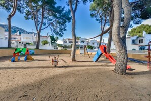 A playground with swings and slides, surrounded by trees and buildings. - Calpe Park, HOUSE WITH TERRACE AND SWIMMING POOL – IDEAL FOR FAMILIES · PARKING  · CALPE (Calpe)