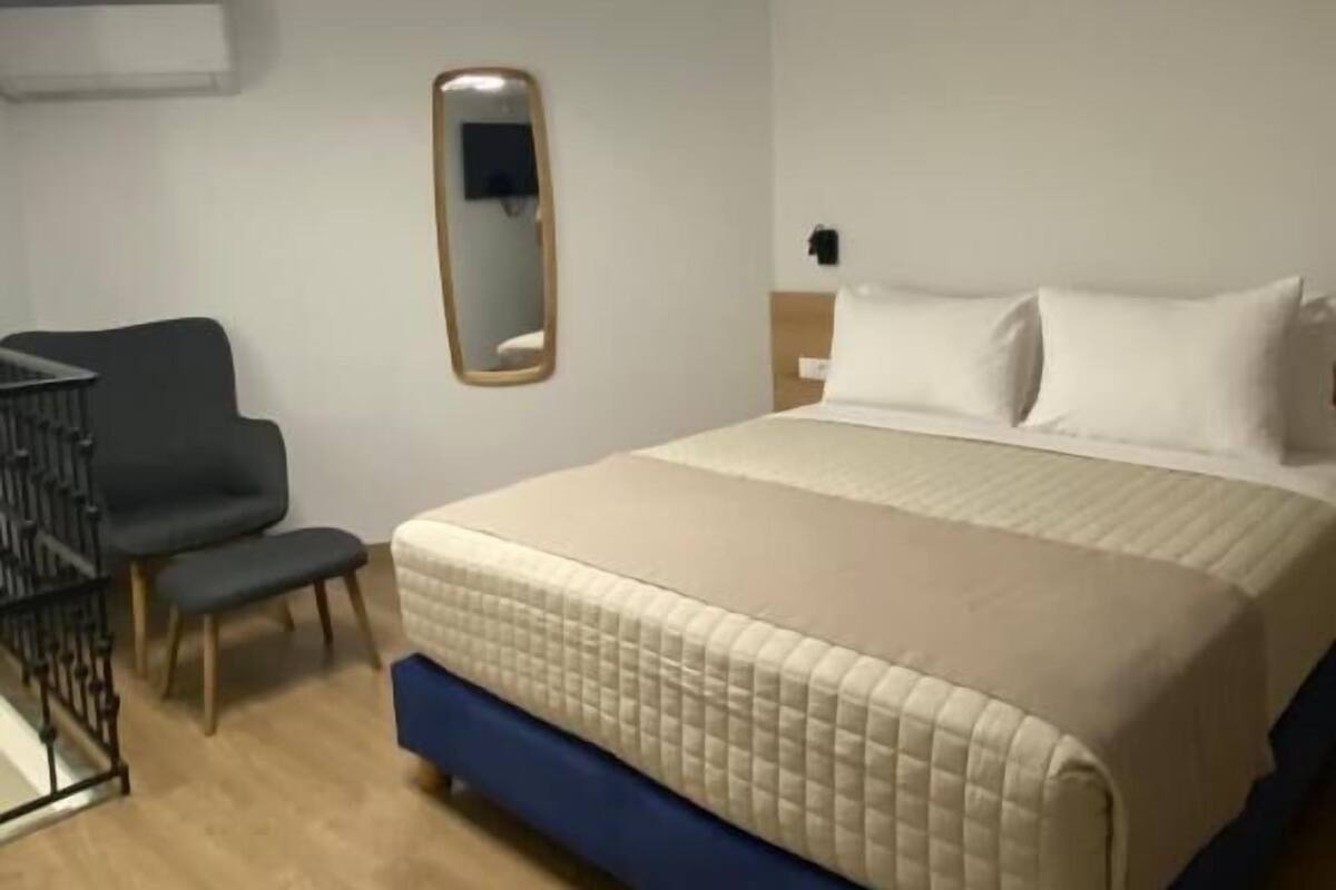 Hotellihuone, jossa on sänky, tuoli, peili ja kattovalaisin.