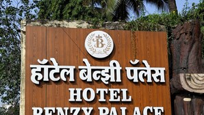 Ein Holzschild für Hotel Benzy Palace mit Auflistung der Annehmlichkeiten: Executive Zimmer, Shine Hospitality, Restaurant & Bankettsaal sowie Catering-Service für Veranstaltungen im Freien.