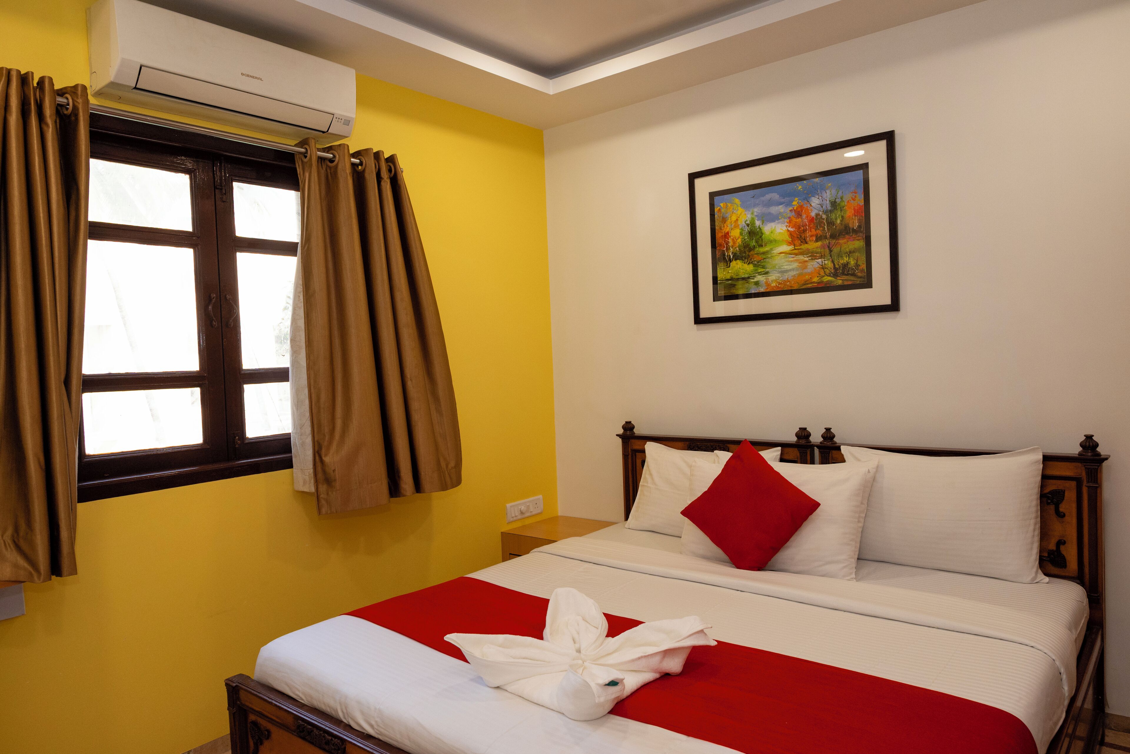 Una habitación de hotel con cama, un cuadro en la pared y aire acondicionado.