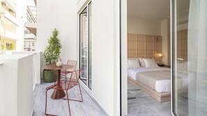 A balcony with a table and chairs, a potted plant, and a view of a bedroom with a bed and nightstand. - Milioni by Oniro (Athens)