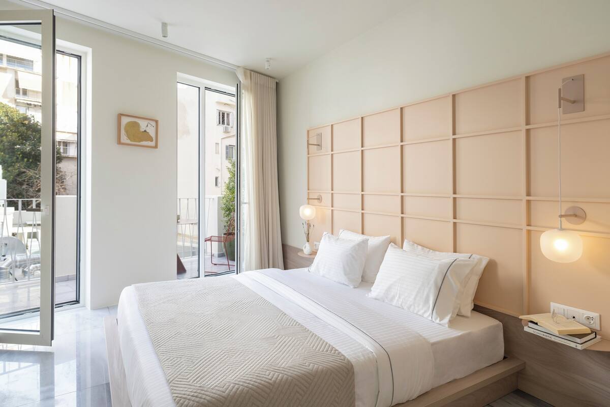 Una habitación de hotel moderna con una cama grande, vistas a través de una puerta corredera y una mesita de noche con una lámpara.