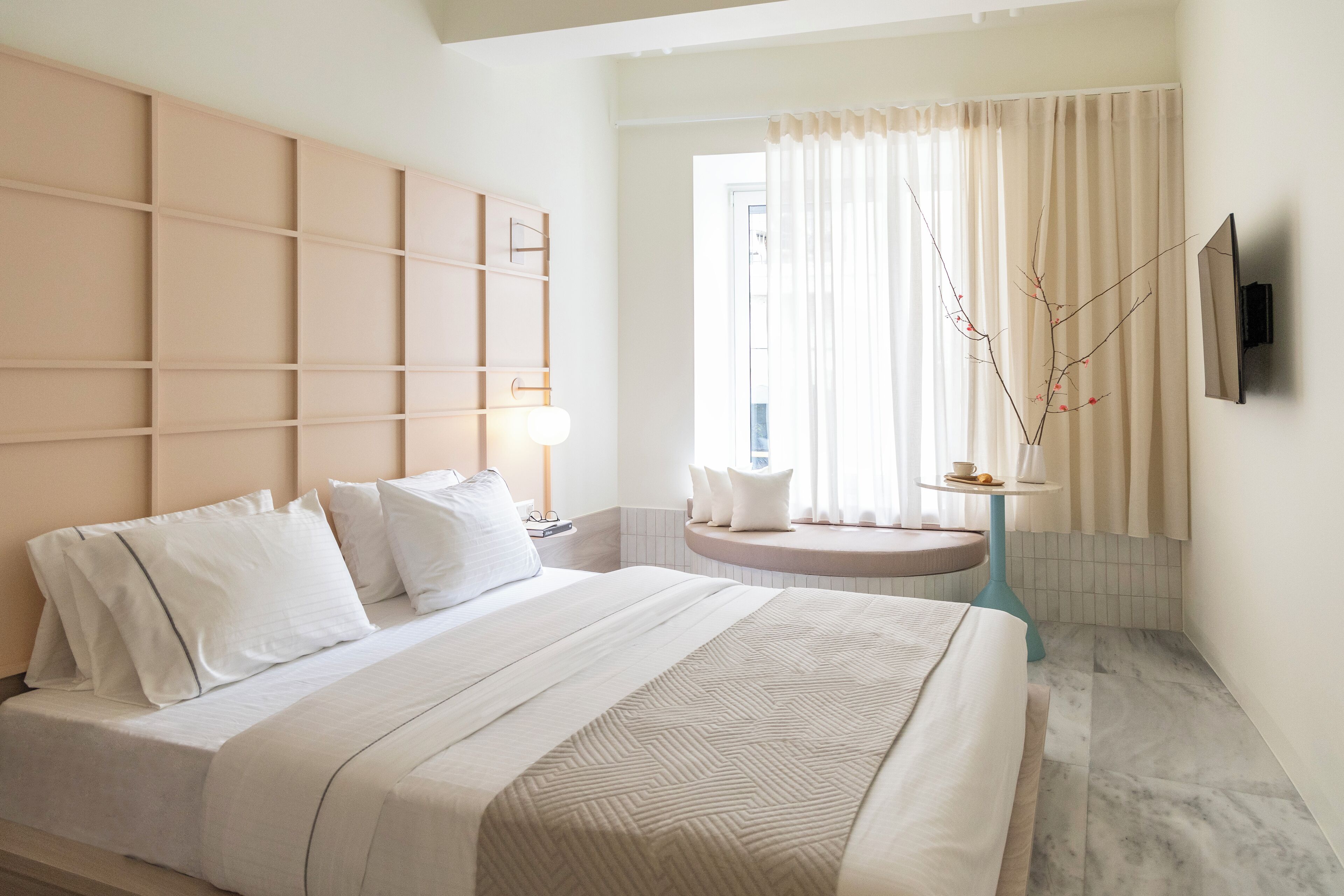 A modern hotel room with a large bed, a built-in headboard, a round table, and a TV mounted on the wall.