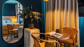 Et moderne hotelværelse med spiseplads, et stort spejl, en airconditionenhed, en vase med blomster og et fjernsyn på væggen.