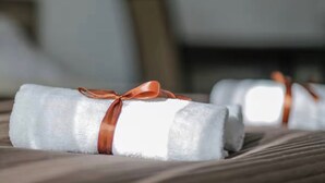 A bed with neatly rolled white towels tied with brown ribbons.