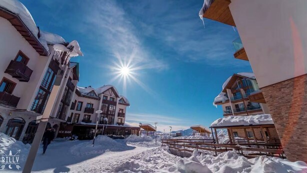 A snow-covered building with a sun shining in the background.