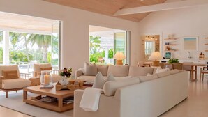 Un salón amplio con un sofá seccional beige grande, una mesa de centro de madera y vistas al exterior a través de ventanas grandes.